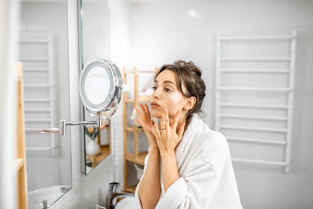 Effective age spot treatments to help you - woman looking on her skin at bathroom F8WWBSG Botox Nottingham Dermal Fillers Beeston West_Bridgford Skin Tag Removal Wart Cheek Fillers Chesterfield Lincoln Leicester Beauty Skin Dermatology Treatments